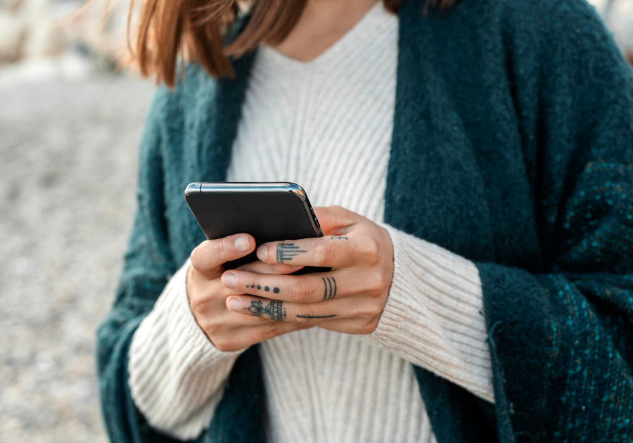 A close up of a lady holding her phone with tattoos on her left hand.