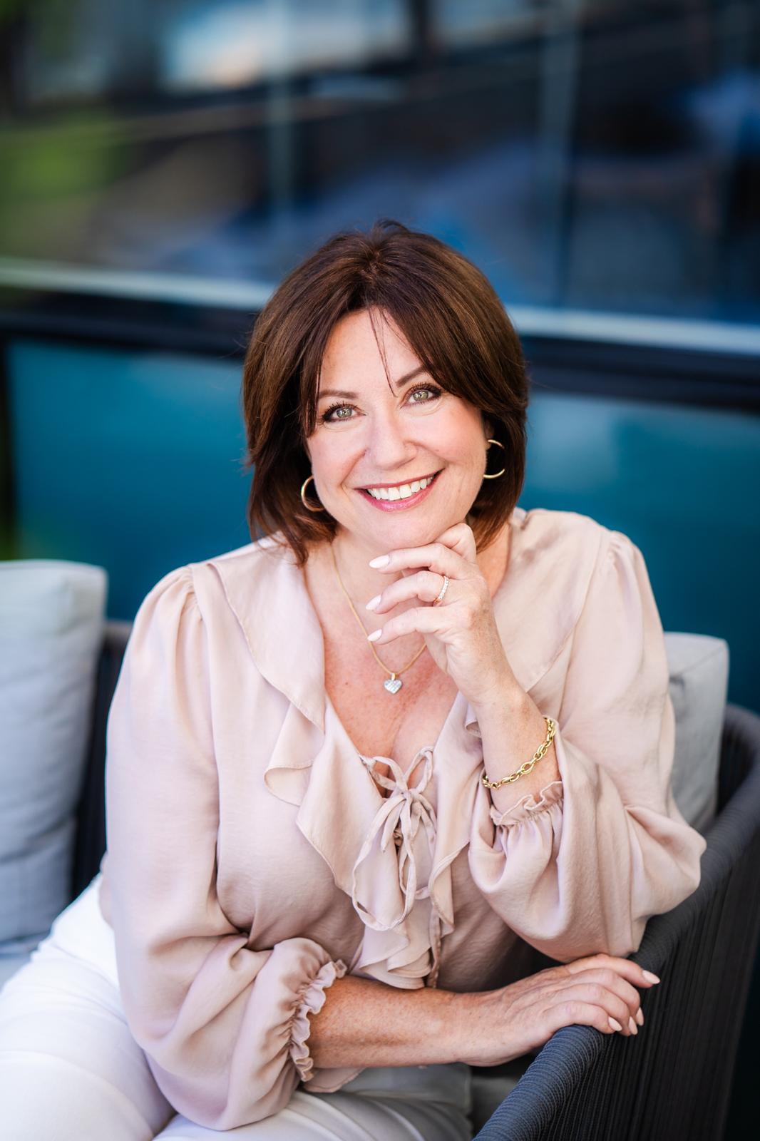 Nikki in a dusty pink coloured top smiling at the camera with a blue background behind her.